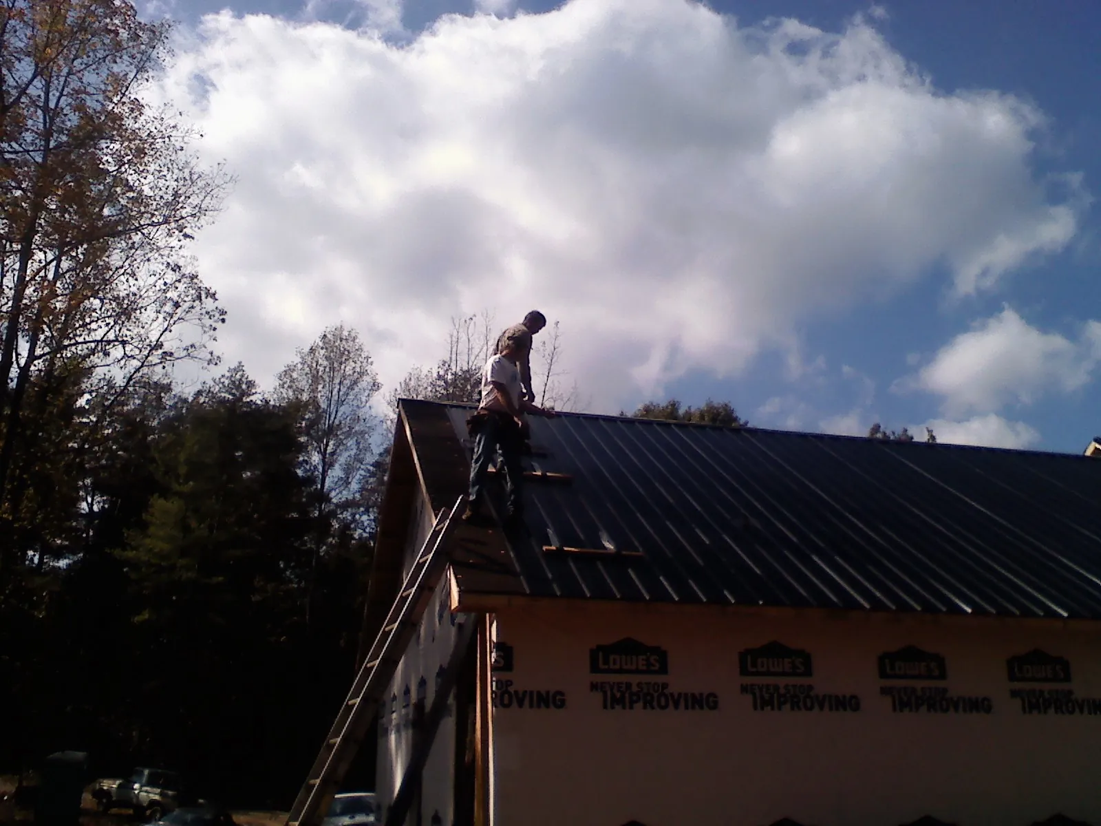 Roofer fastening dark metal panels high against a cloudy sky, from a Roof Inspection job in Beaumont